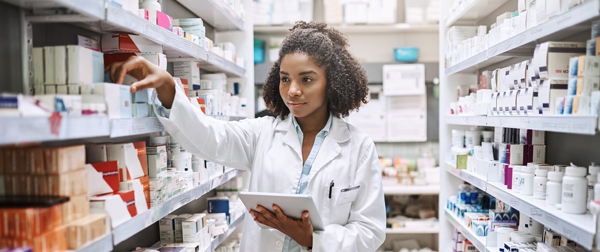Female Pharmacist looks at medication boxes on shelf